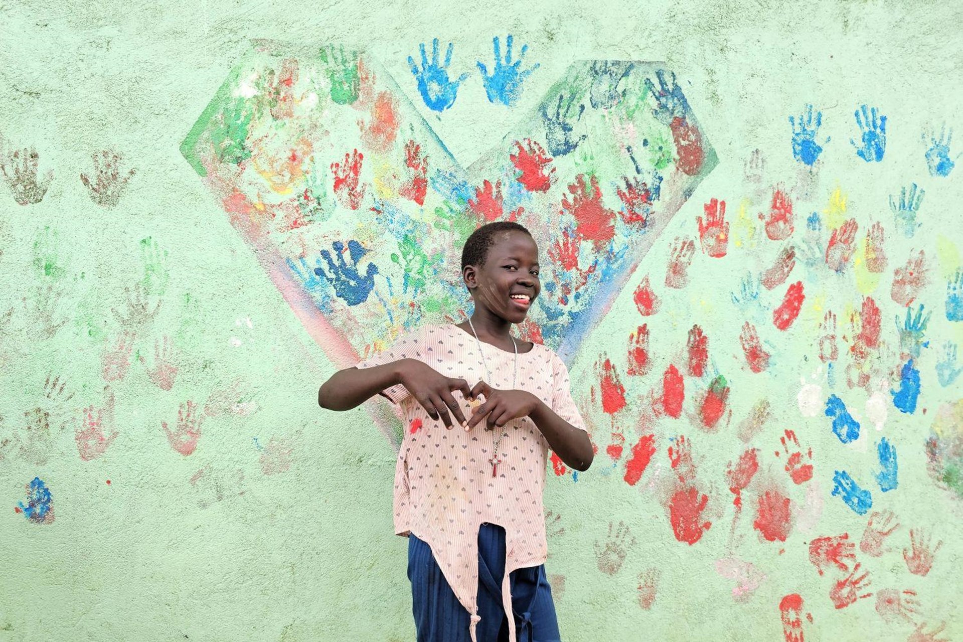 Ein Mädchen steht vor einer bunt bemalten Hauswand und formt mit den Händen ein Herz.